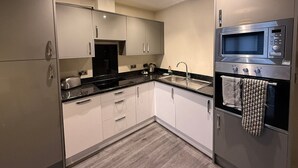 Uma cozinha moderna com armários brancos, bancada preta, eletrodomésticos de aço inoxidável e piso de madeira.