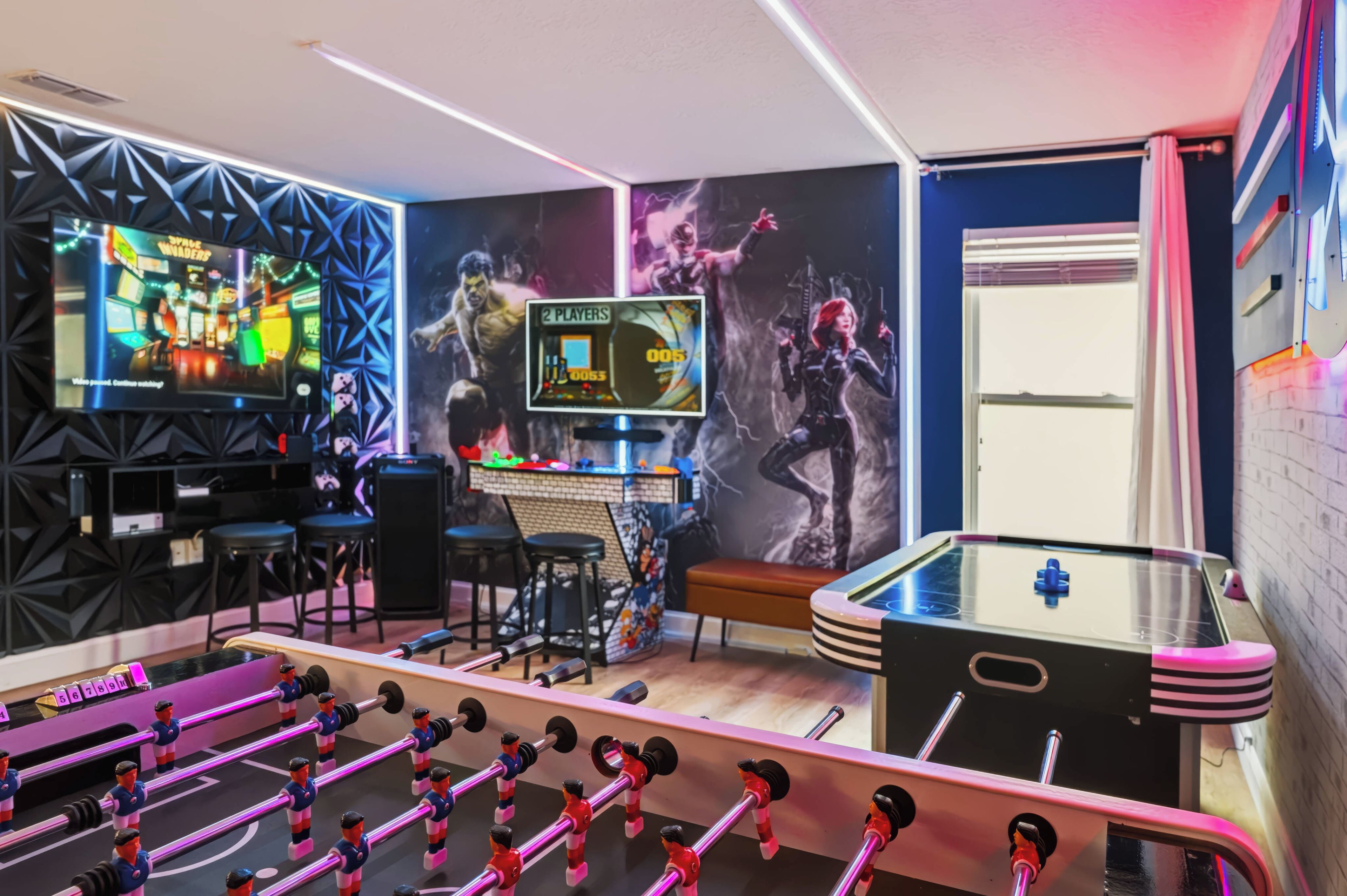 Ein Zimmer mit einem Tischfußballtisch, einer Spielkonsole und einer Wand mit einem großen Poster.