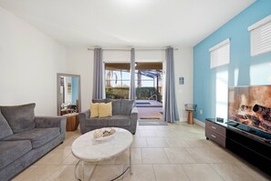 Ein Wohnzimmer mit grauem Sofa, einem runden Couchtisch und einem Fernseher auf einer Holzkommode.