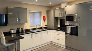 A modern kitchen with stainless steel appliances, a bar stool, and a window with blinds. - Contemporary 2-bedroom perfect for Families (London)