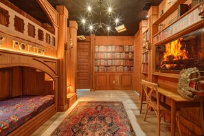 A cozy library with wooden bookshelves, a fireplace, and a bed with a 'Harry Potter' themed headboard. - 8BR house sleeps 22 with pool table (Kissimmee)