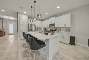 A modern kitchen with white cabinets, stainless steel appliances, and a central island with bar stools. - 8BR house sleeps 22 with pool table (Kissimmee)