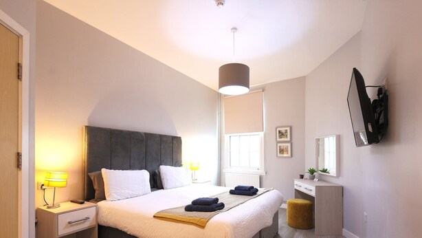 Une chambre à coucher moderne, avec un lit, des tables de chevet, un bureau, un miroir et un téléviseur fixé au mur.