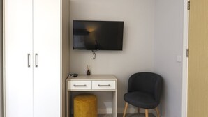 Une pièce avec une armoire blanche, un bureau sur lequel est posée une télévision, une chaise noire et un pouf jaune rond.