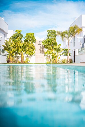 A swimming pool with a clear blue water surface, surrounded by lush green tropical plants and white buildings. - Pilar Prime Penthouse, Rooftop & Pool Experience by OYOOSTAYS (Pilar de la Horadada)