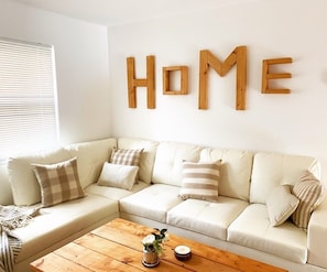 Una sala de estar con un sofá blanco, una mesa de centro de madera y una pared con la palabra "HOME" en letras de madera.
