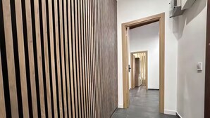 En hall med en väggpanel av träribbor, ett mörkt klinkergolv och en trädörr längst ner.