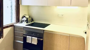 Una cucina compatta con mobili bianchi, forno integrato e finestra con vista.