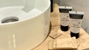 Ett badrum med ett vitt handfat, en svart kran och två flaskor med badgel och schampo från serien Green Tea Collection, placerade på ett träbricka.