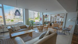 Een moderne woonkamer met een bank, salontafel en stoelen, grote ramen met uitzicht op de stad, en een eethoek met een tafel en stoelen.