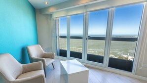 Een kamer met een groot raam, twee stoelen, een klein tafeltje en een blauwe muur.