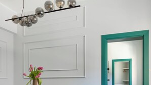 Un espace repas moderne avec une table ronde, deux chaises rembourrées, un vase de fleurs et un luminaire au plafond au design original.