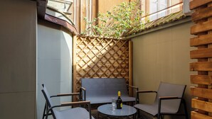 Une cour avec un sol en pierre, une table entourée de chaises et une bouteille de vin.