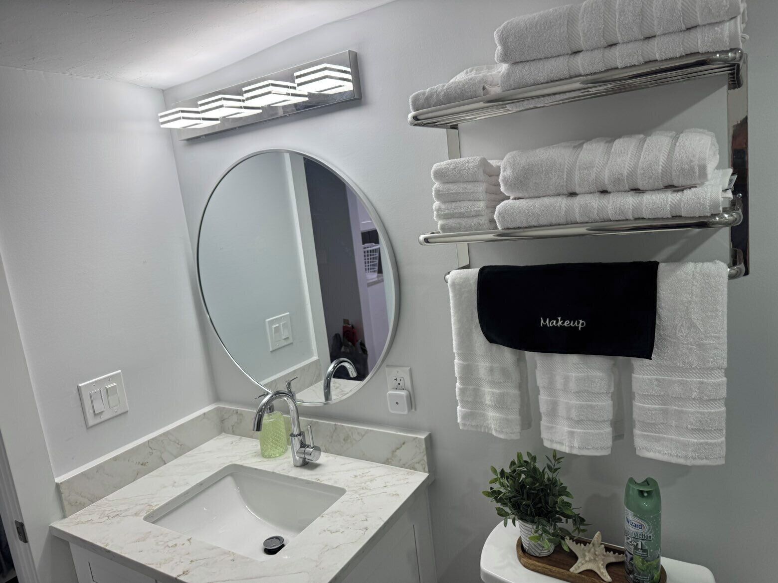Un bagno moderno con un ampio specchio, un lavabo in marmo bianco e diversi asciugamani bianchi su un portascopevoli.