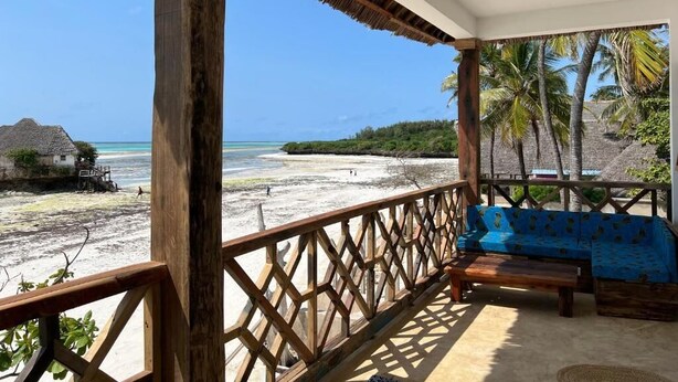 Una terraza de madera con techo de paja, un sofá azul y vista a una playa y al océano.