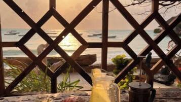 A breakfast table with fruit, a pitcher of orange juice, and a cup, overlooking the ocean at sunset.