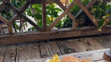 A wooden table with a burger, fries, and salad, set against a wooden fence overlooking a beach.