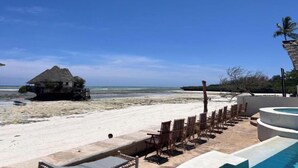 Un complejo turístico en la playa con piscina, sillas de descanso y una estructura de techo de paja.