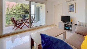 A modern living room with a sofa, a TV, and a balcony with chairs. - Moderne 2 Pieces Climatise Avec Terrasse A1b230 (Cannes)