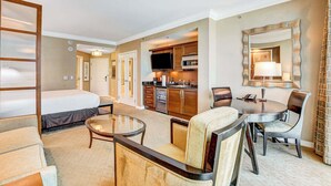 Habitación de hotel con cama, una pequeña mesa de comedor con sillas, kitchenette y un espejo grande.