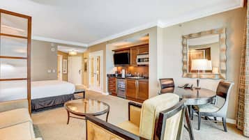 A hotel room with a bed, a small dining table with chairs, a kitchenette, and a large mirror.