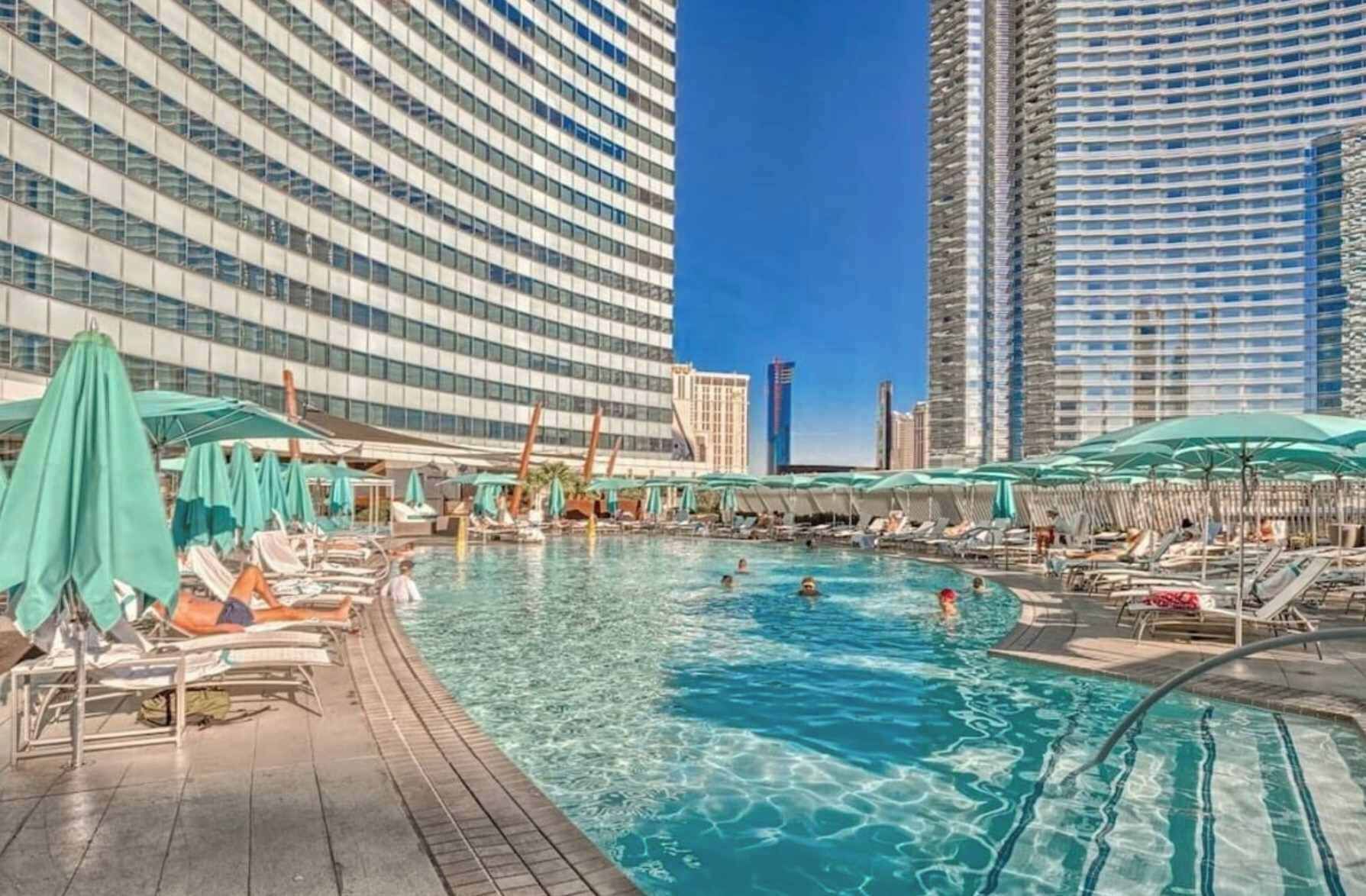 A hotel pool area with sun loungers and umbrellas, surrounded by high-rise buildings.