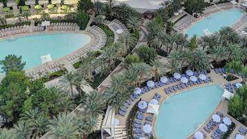 A resort with two large swimming pools, surrounded by palm trees and sun loungers.