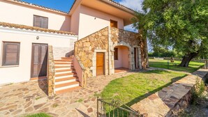Uma casa de dois andares com uma escadaria de pedra que leva a uma porta de madeira, cercada por um muro de pedra e uma área gramada.