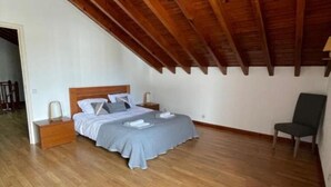 Una camera da letto con soffitto in legno, un letto con copriletto grigio, un comodino e una sedia.