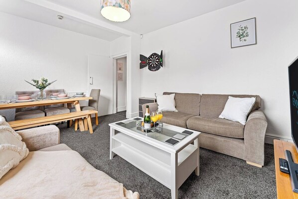A modern living room with a sofa, a coffee table, a dining table with chairs, and a television.
