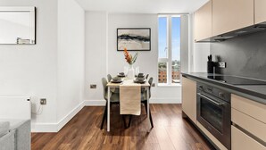 Une cuisine moderne dotée d’un four encastré, un coin repas avec une table dressée pour quatre personnes et une grande fenêtre offrant une vue sur la ville.