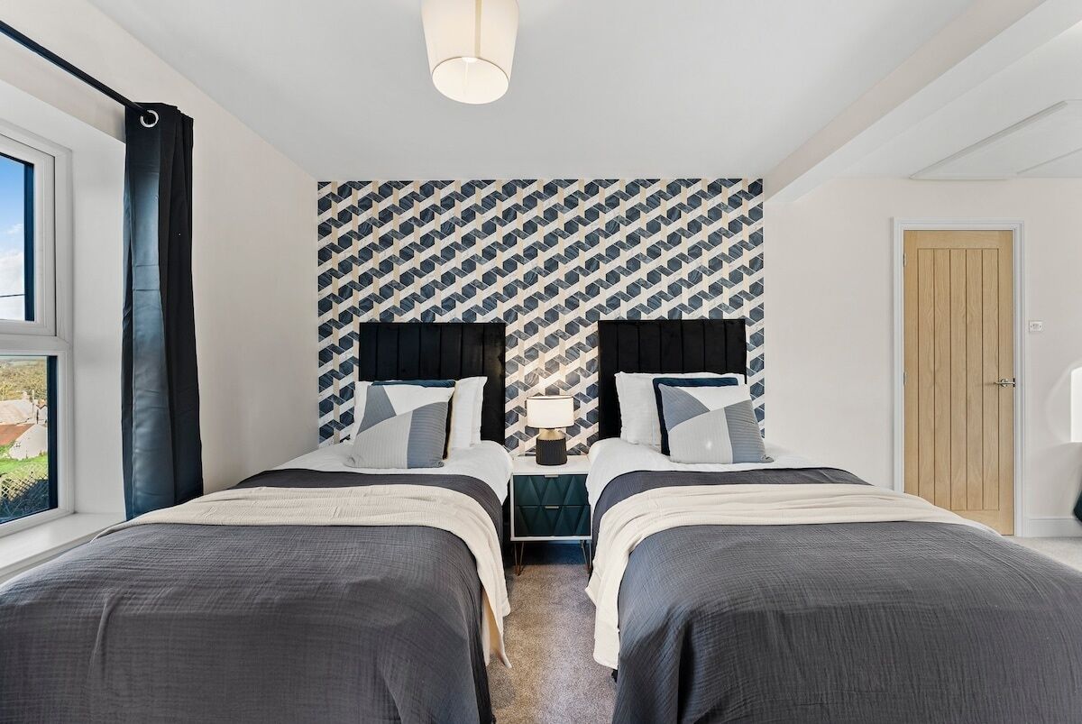 A modern bedroom with two beds, a patterned wall, and a window.