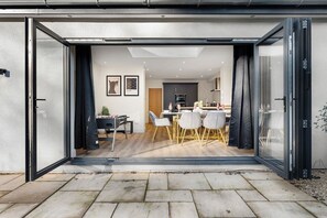 A modern kitchen with dark cabinets, a central island, and a dining area with a table and chairs. - The Bath Cotswolds Rural Retreat - Sleeps 14 (Bath)