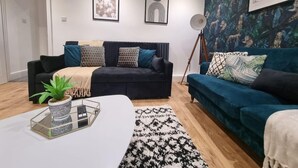 Uma sala de estar moderna com um sofá azul escuro, uma mesa de centro branca com uma planta e um tapete estampado.
