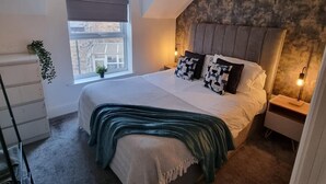 Quarto com uma cama grande, um claraboia, vista da cidade, cômoda e mesa de cabeceira com abajur.