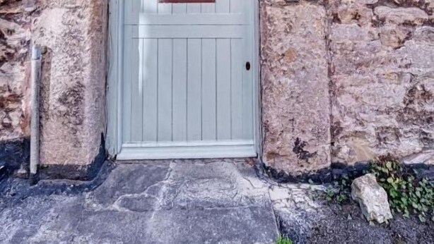 Ein Steinhaus mit einer hellblauen Tür, einem kleinen Fenster und einem Schild, auf dem 'Batch Cottage 183' steht.
