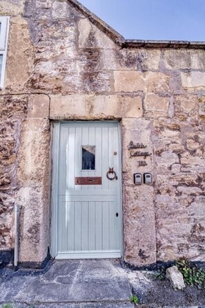A stone building with a light blue door, a small window, and a sign reading "Batch Cottage 183".
