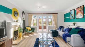 A modern living room with a fireplace, a sofa, a glass coffee table, and a TV. - Large 6 Bedroom Cambridge Abode (Cambridge)