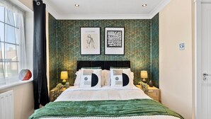 Une chambre d’hôtel avec un lit, deux tables de chevet, une fenêtre avec des rideaux et deux œuvres d’art encadrées accrochées au mur.