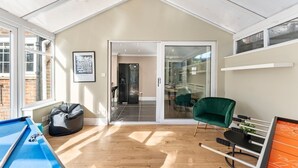 Un salon moderne avec une table de billard, un fauteuil vert et une porte vitrée donnant sur un coin repas.
