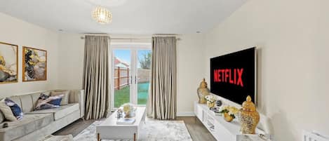 Una sala de estar moderna con un sofá, una mesa de centro y un televisor de pantalla plana mostrando 'NETFLIX'.