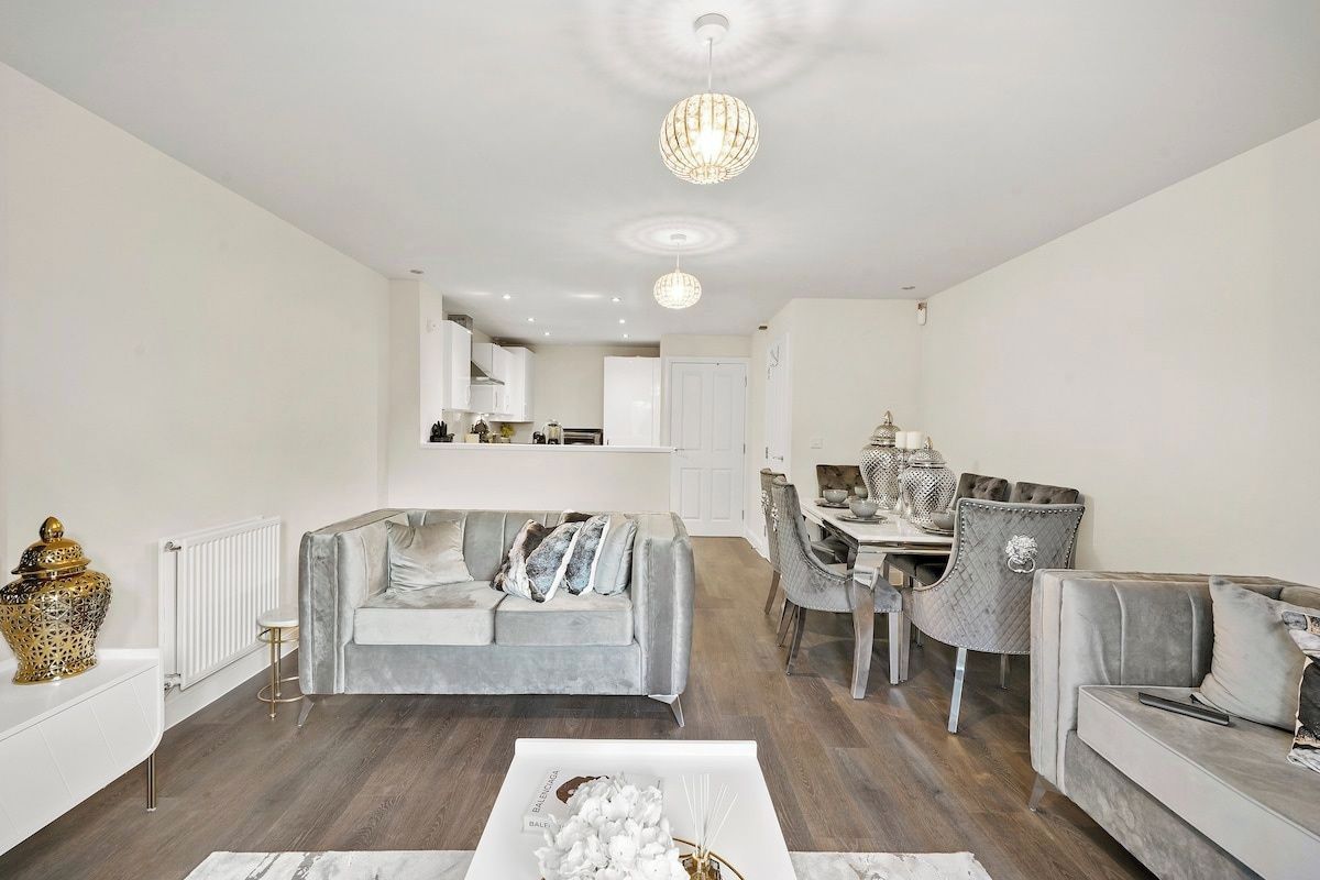 A modern living room with a grey sofa, a coffee table, and a dining area with chairs and a table.