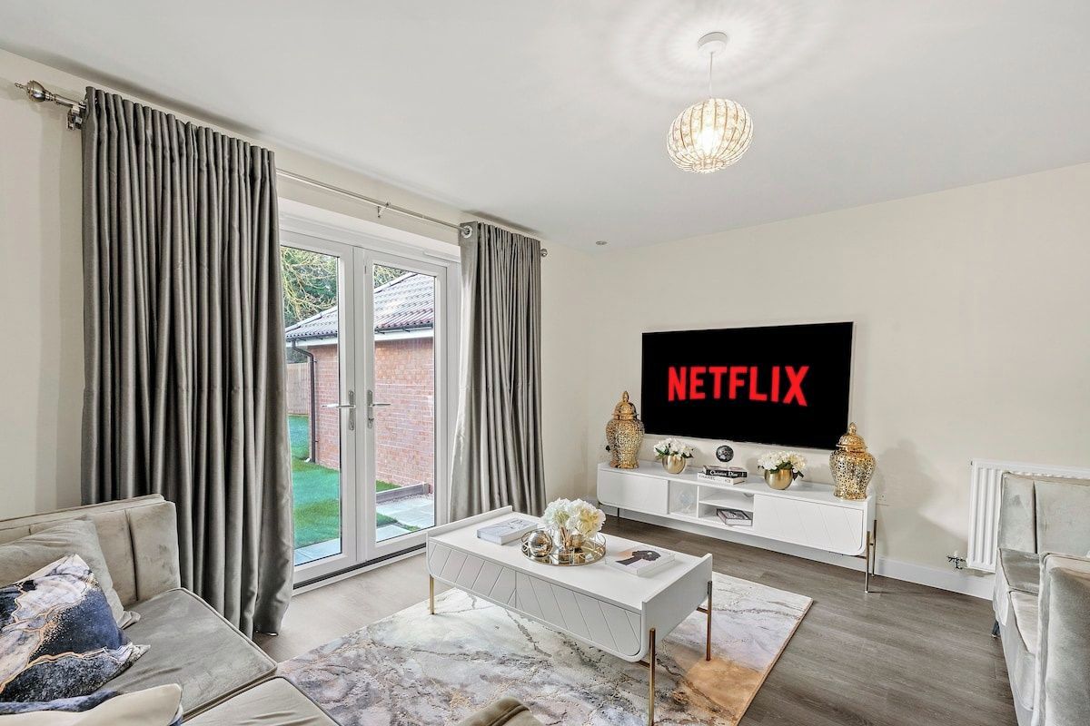 Een moderne woonkamer met een flatscreen televisie, een bank, een salontafel en een schuifpui die uitkomt op een tuin.