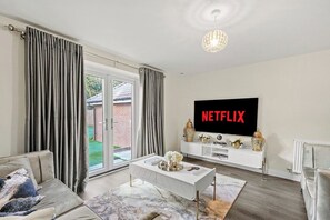Ein modernes Wohnzimmer mit einem Flachbildfernseher, einer Couch, einem Couchtisch und einer Glasschiebetür, die zu einem Garten führt.