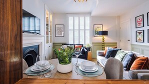 Un comedor con una mesa de madera dispuesta para dos personas, una planta en maceta y una lámpara de araña moderna.