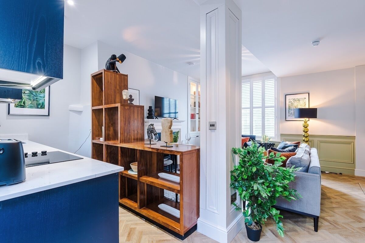 Een moderne keuken met een ingebouwde kookplaat, houten planken en een zithoek met een grijze bank en een potplante.