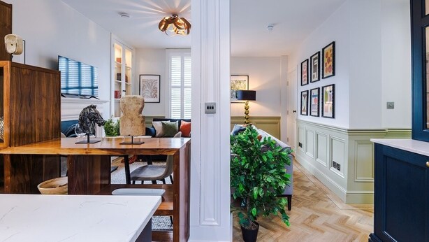 Una sala de estar moderna con comedor, una planta grande y una escalera que lleva a otro nivel.