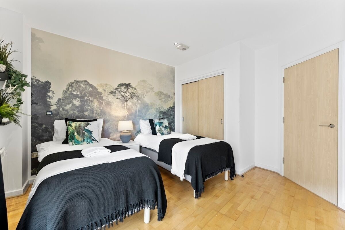 Een kamer met twee bedden, een muurschildering, een houten deur en een potplant.