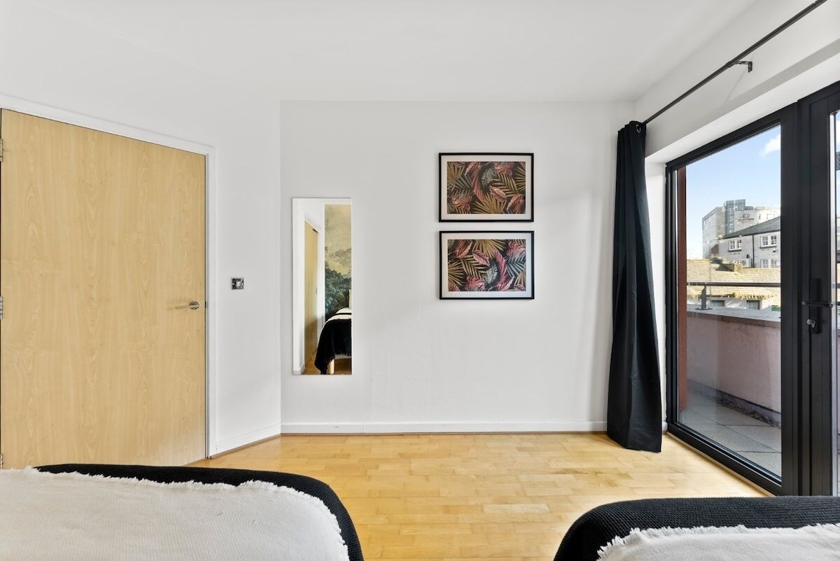 A modern room with a wooden floor, a large window with a view of buildings, and two framed artworks on the wall.
