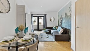 Een moderne woonkamer met een bank, een eettafel voor vier personen, een ronde salontafel en een grote wandklok.
